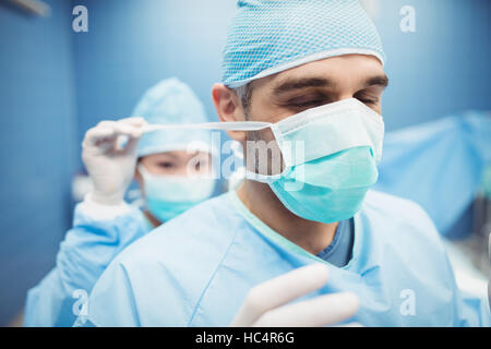 Aider un infirmier chirurgien en attachant un masque chirurgical Banque D'Images