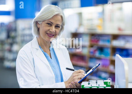 Pharmacien writing on clipboard in pharmacy Banque D'Images