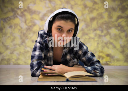 Jolie teen girl à chemise à carreaux fille couchée dans le casque et la lecture d'un livre Banque D'Images