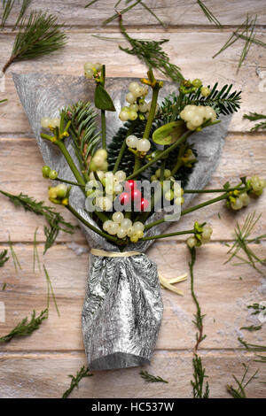 Capture d'un grand angle d'un bouquet de gui arrangé enveloppée dans un tissu argenté sur une surface en bois avec quelques brindilles de plantes et les branches, on a rustic Banque D'Images