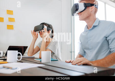 Jeune homme et femme assise à une table et à l'aide de lunettes de réalité virtuelle. L'équipe d'affaires à l'aide de casque de réalité virtuelle en réunion de bureau. Banque D'Images