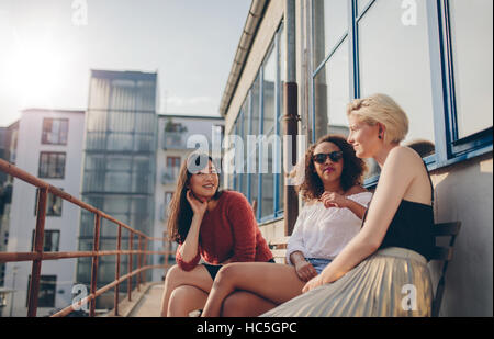 Trois jeunes amis féminins assis sur un balcon. Les femmes de détente en plein air et le chat. Banque D'Images