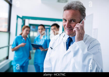 Portrait of smiling doctor talking on mobile phone in corridor Banque D'Images