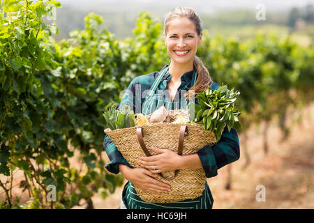 Portrait of happy female farmer holding un panier de légumes Banque D'Images