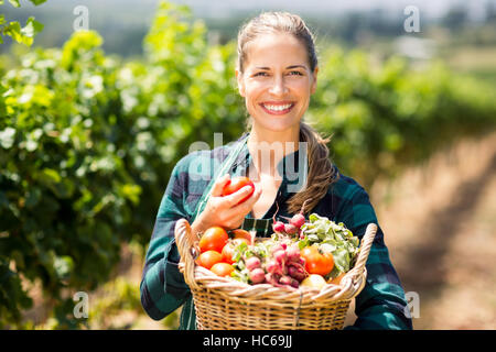 Portrait of happy female farmer holding un panier de légumes Banque D'Images