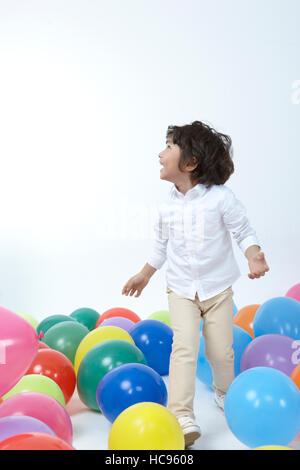 Vue latérale du smiling boy playing in colorful balloons Banque D'Images