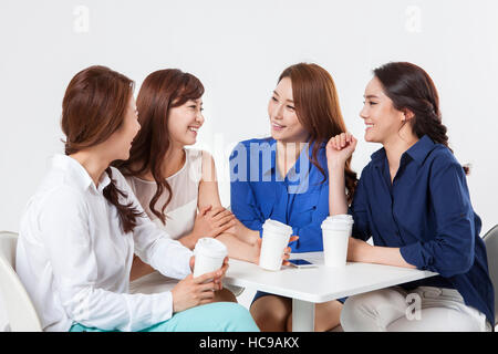 Quatre jeunes femmes d'souriant avec du café à emporter parle table Banque D'Images