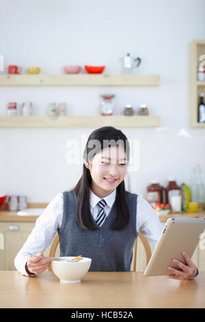 Portrait of smiling middle school girl eating cereal using tablet Banque D'Images