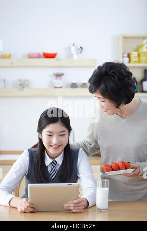 Smiling middle school girl using tablet and her smiling mother Banque D'Images