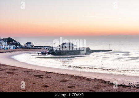 Aube du ciel brisant sur la mer à Broadstairs avec le port et la plage à l'avant-plan. Ciel clair avec couche de nuages sur l'horizon. Mer calme. Banque D'Images