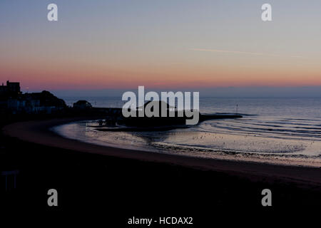 Aube du ciel brisant sur la mer à Broadstairs avec le port et la plage à l'avant-plan. Ciel clair avec couche de nuages sur l'horizon. Mer calme. Banque D'Images