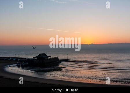 Aube du ciel brisant sur la mer à Broadstairs avec le port et la plage à l'avant-plan. Ciel clair avec couche de nuages sur l'horizon. Mer calme. Banque D'Images
