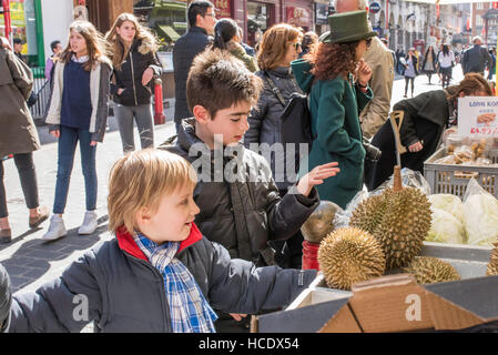 Deux jeunes garçons à la toucher et fruits exotiques hérissés sur un étal au marché dans une rue animée, Chinatown, Soho. Banque D'Images