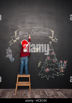 Happy child wearing hat standing près de selles sur arbre de Noël tout en s'appuyant sur tableau noir. Banque D'Images