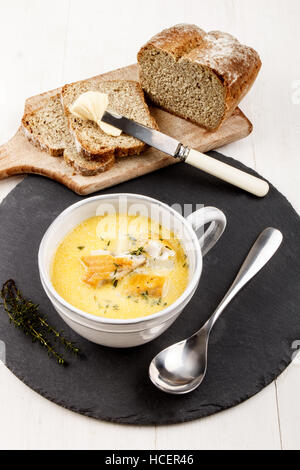 Soupe de poissons traditionnels écossais, Cullen Skink, avec les pommes de terre dans une tasse d'argile gris sur une ardoise ronde et des soda bread sur planche de bois Banque D'Images