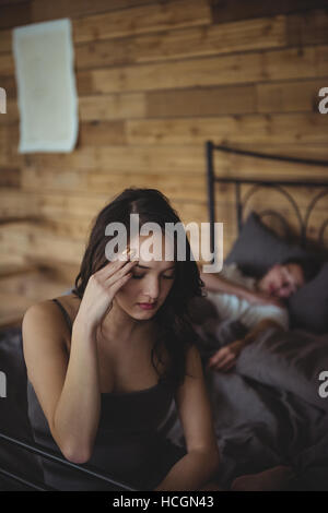 Femme assise en colère sur un lit tandis que l'homme dort en arrière-plan Banque D'Images