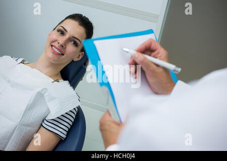 Doctor writing on clipboard pendant que le patient couché sur lit de soins dentaires Banque D'Images