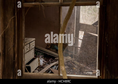 Regardant à travers la fenêtre brisée de la fenêtre d'une maison abandonnée avec une commode et mur manquant Banque D'Images