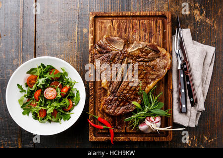 T-bone steak grillé avec de la salade avec des tomates cerises et de la roquette sur le service à bord sur fond de bois Banque D'Images