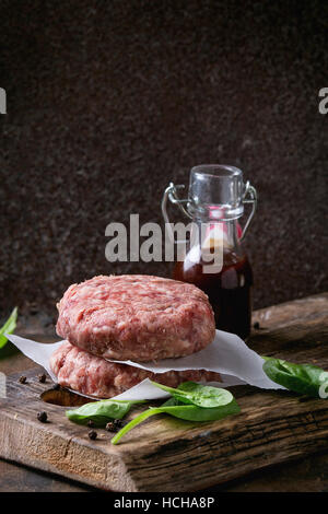 Ingrédients pour faire de hamburger. Escalope de boeuf hamburger cru, deux petits pains, oignon frit, épinards frais et sauce ketchup sur planche sombre plus vieux woode Banque D'Images