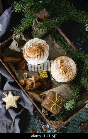 Latte épicé à la citrouille avec crème fouettée et de cannelle dans deux verres debout dans planche de bois avec du textile et de décoration de Noël et de sapin autres Banque D'Images