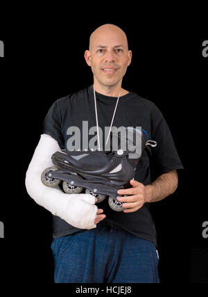 Jeune homme portant un bras blanc brillant exprimés, la tenue d'une inline skate une effraction son bras dans un accident de patin à roues alignées, isolé sur fond noir Banque D'Images