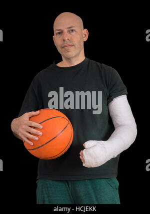 Jeune homme portant un bras blanc brillant, en tenant une basket-ball après avoir cassé le poignet dans un match de basket-ball de l'automne, isolated on black Banque D'Images