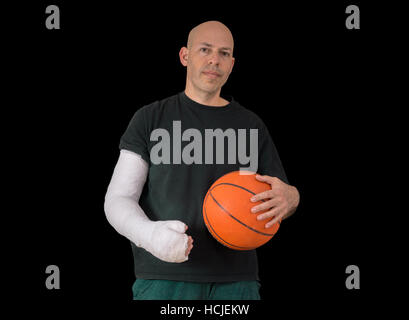 Jeune homme portant un bras blanc brillant, en tenant une basket-ball après avoir cassé le poignet dans un match de basket-ball de l'automne, isolated on black Banque D'Images