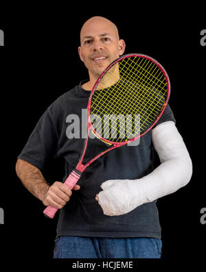 Jeune homme tenant une raquette de tennis après avoir cassé le poignet dans un jeu de tennis, arborant un moulage du bras blanc brillant, isolé sur fond noir Banque D'Images