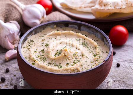 Dans l'hummus accueil bol conçu avec de l'ail et les tomates autour. Banque D'Images