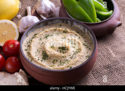 Dans l'hummus accueil bol conçu avec de l'ail et les tomates autour. Banque D'Images