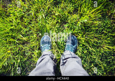 Les pieds mâles dans les chaussures de sport bleu debout sur l'herbe d'été vert clair Banque D'Images