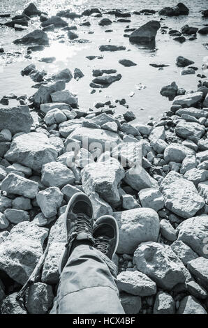 Les pieds mâles dans les chaussures de sport en toile bleu debout sur les zones côtières un sol rocailleux. Voyage lifstyle verticale arrière-plan. Filtre photo, dans les tons bleus Banque D'Images