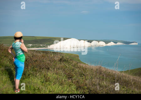 Une femme regarde vers les Sept Soeurs en marchant dans les South Downs Way, Parc National des South Downs, East Sussex, UK Banque D'Images