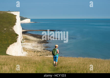 Une femme marche le long des falaises près de Beachy Head avec une vue sur les Sept Soeurs de côte, le Parc National des South Downs, UK Banque D'Images