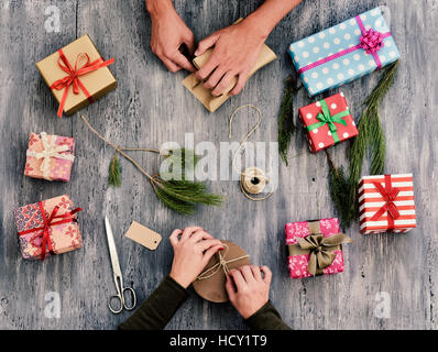 Capture d'un grand angle d'une jeune femme de race blanche et un jeune homme de race blanche, cadeaux sur une table en bois gris rustique plein de cadeaux et de brindilles et naturel Banque D'Images