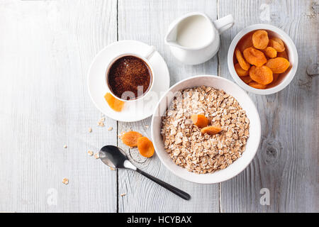 Petit déjeuner de gruau avec des abricots séchés et tasse de café noir sur une table en bois blanc Banque D'Images