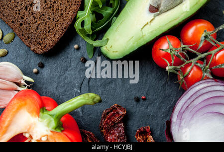 Snack-ingrédients : pain, avocat, roquette, Tomates, ail, poivrons, tomates séchées au soleil sur fond noir en noir avec une copie de l'espace dans le centre Banque D'Images