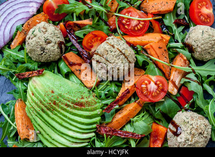 Salade Vegan : avocat, la patate douce, de lentilles escalopes, tomates, roquette, oignons sur fond noir en noir avec une copie de l'espace dans le centre Banque D'Images