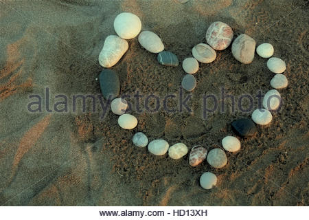 Pierre galets coeur d'amour sur une plage au coucher du soleil comme Rhodes jette une lumière douce sur le sable. Banque D'Images