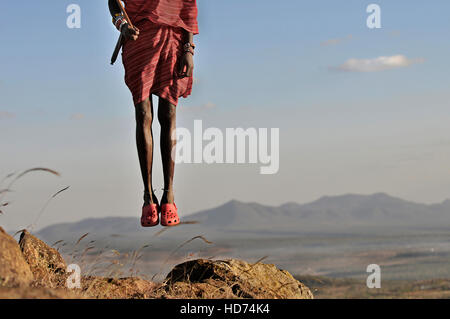 Guerrier massaï sautant avec Crocs et belles en arrière-plan. Le Kenya, l'Afrique. Banque D'Images