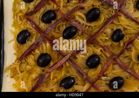 Réseau d'anchois et les olives sur les oignons cuits sur la pâte feuilletée au moment de faire pissaladiere, pour la cuisson de près. Banque D'Images