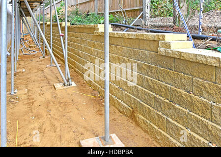 La construction à sec à l'aide de blocs de béton creux rempli de gravier d'un mur de soutènement en forme comme limite de nouvelle maison pour retenir la terre dans le jardin des voisins UK Banque D'Images