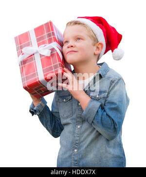 Jeune garçon curieux Wearing Santa Hat Holding Christmas Gift isolé sur un fond blanc. Banque D'Images