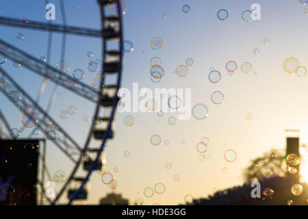De nombreuses bulles flottant avec un arrière-plan flou de la roue géante contre un ciel de coucher du soleil Banque D'Images