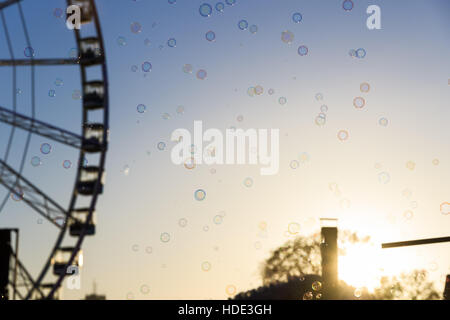 De nombreuses bulles flottant avec un arrière-plan flou de la roue géante contre un ciel de coucher du soleil Banque D'Images