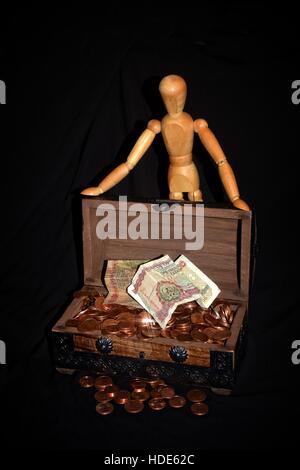 Figure en bois debout derrière une boîte en bois plein d'argent - pièces de monnaie sur fond noir Banque D'Images