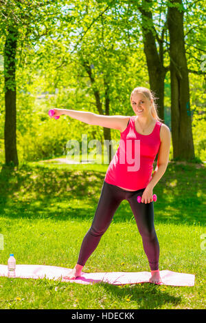 Jeune femme enceinte faisant des exercices avec haltères courtes dans le parc Banque D'Images