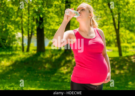 Portrait d'une femme enceinte de boire de l'eau fraîche d'une bouteille dans le parc Banque D'Images