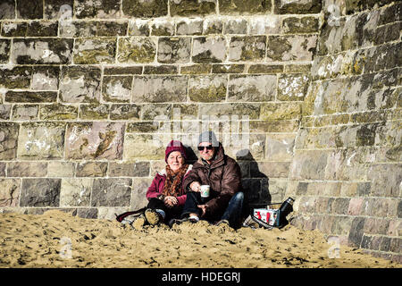 Se détendre avec une fiole de thé sur la plage du Barry Island, Vale of Glamorgan, Pays de Galles, où un ciel dégagé et un soleil brillant dominent le littoral sud du Pays de Galles que décembre les températures continuent à être doux. Banque D'Images